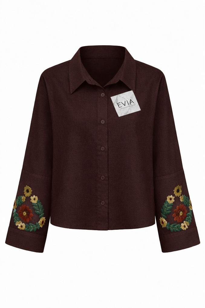 A dark brown button-up shirt jacket by Evia, featuring floral embroidery on the lower sleeves and a white brand label on the chest, shown against a plain white background.