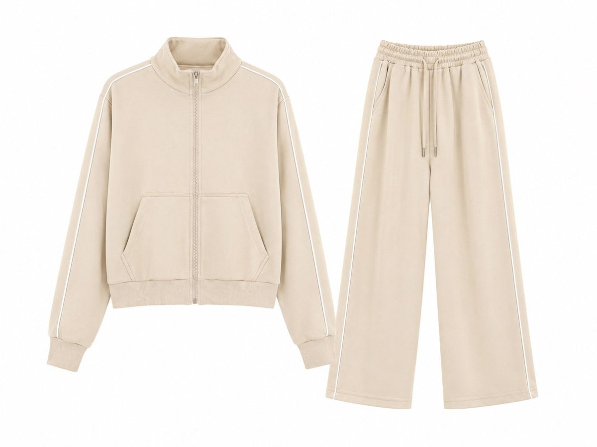 A two-piece beige tracksuit set featuring a cropped zip-up jacket with white stripe details on the sleeves and front pockets, paired with matching wide-leg sweatpants with white side stripes and a drawstring waist.