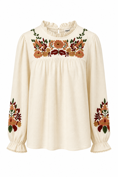 An off-white long-sleeve blouse with ruffled trim at the neck and cuffs, featuring colorful floral embroidery across the chest and on the sleeves.