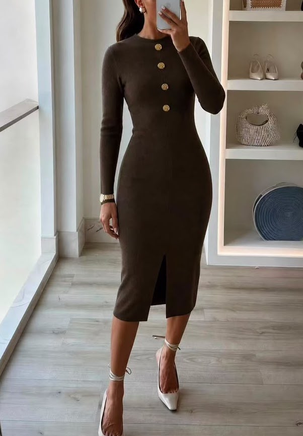 A woman modeling a fitted long-sleeve midi dress in dark brown with gold buttons down the front, standing in a bright indoor room with light wood flooring and white shelving.