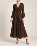A woman models a long-sleeve, dark brown lace midi dress with a wrap-style V-neck and a matching fabric tie belt at the waist, paired with black strappy high-heeled sandals against a plain beige studio background.